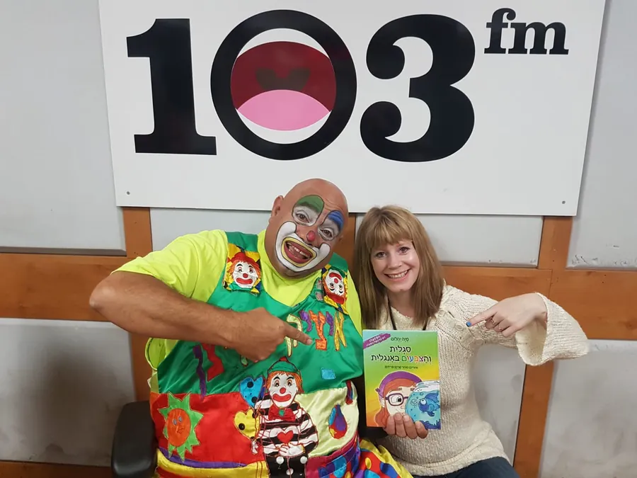 מיה יהלום עם איציק הליצן באולפן 103FM, מחזיקה את הספר סגלית והצבעים באנגלית